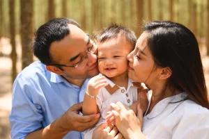 Loving parents and baby embracing and kissing on cheek at park