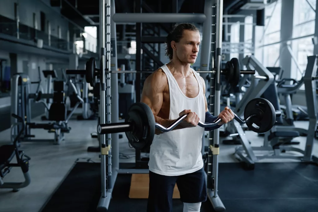 Man athlete training muscles with barbell during physical workout in sport gym