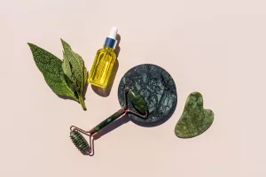 Natural cosmetic massage oil, roller massager and natural jade scraper on a beige background.