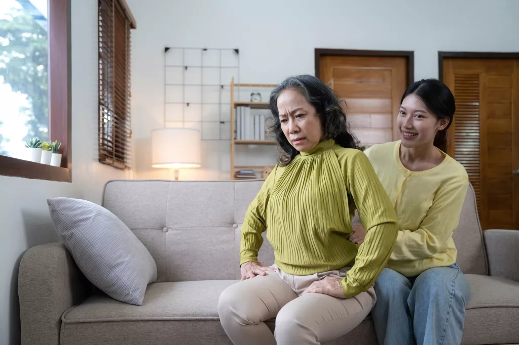 Asian daughter giving an elderly mother a relaxing massage while sitting on the sofa