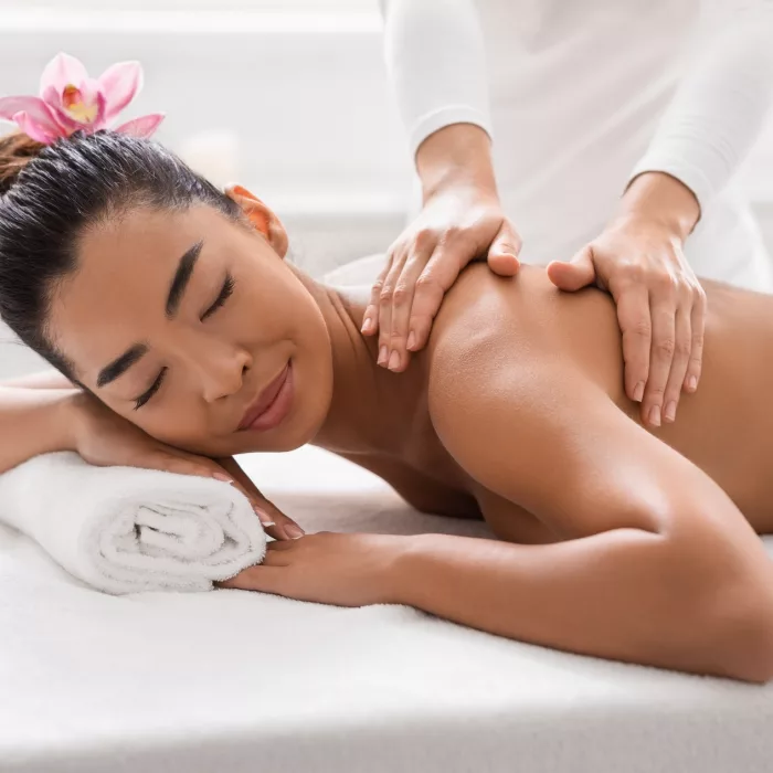 Relaxed Asian Woman Pampering Herself With Body Massage In Spa Salon